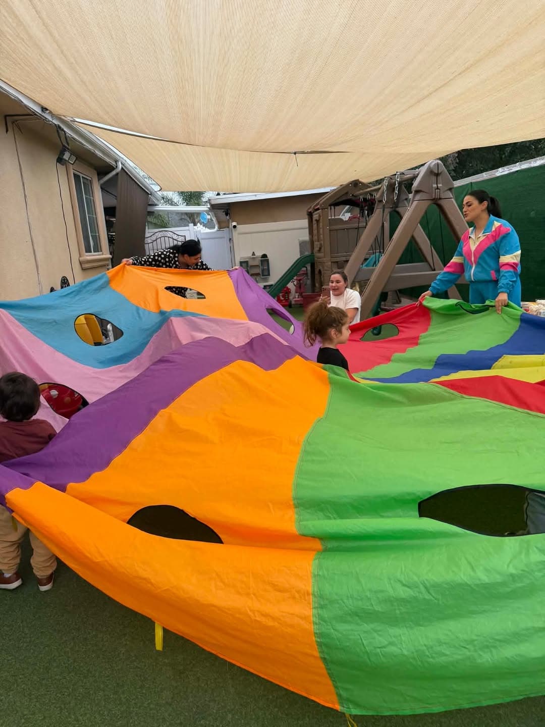 Children and teachers playing under a colorful parachute outdoors